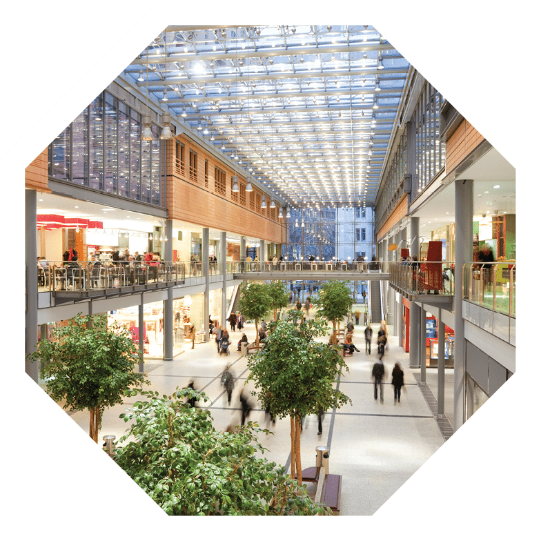 Image taken inside a shopping mall. There are lots of people walking around going to stores, buying things and consuming food and beverages. There are two floors with shops and boutiques. The ceiling is glass. The architecture is very modern and new and the general feel of the images is bright, clean, safe and positive.